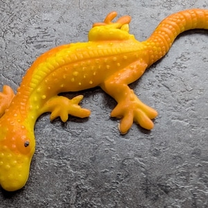 May include: A detailed, orange and yellow lizard figurine with a textured surface. The reptile has a long tail, four legs, and a detailed head. The figurine is a vibrant, eye-catching decorative item.