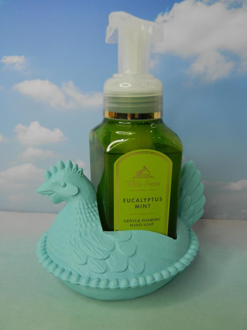 Peut inclure: Un flacon de savon pour les mains vert avec une pompe blanche est plac&eacute; dans un support en forme de poulet bleu clair. L'&eacute;tiquette du savon indique "Eucalyptus Mint Gentle Foaming Hand Soap". Le support a un motif de plumes d&eacute;taill&eacute;.