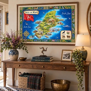 May include: A framed illustrated map of the Isle of Man featuring the red triskelion flag, surrounding Irish Sea, and local wildlife icons. The map is displayed above a wooden console table with a triskelion sculpture and books.