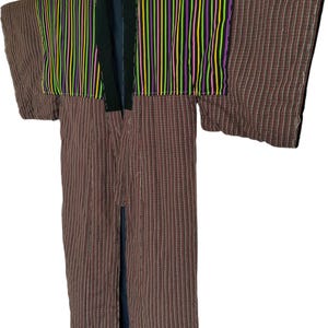 May include: A brown and red striped kimono with a colorful striped panel across the shoulders. The panel features vertical stripes in yellow, green, pink, and purple. The kimono has a black collar and is hanging on a white hanger.