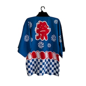 May include: A blue Japanese festival coat, or happi coat, with a bold red graphic on the back. The coat features white swirl designs, a red and white pattern, and a checkered pattern at the bottom. The coat is hanging on a black hanger.