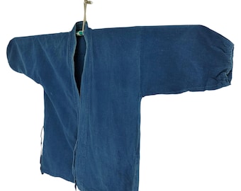 May include: A vintage indigo blue jacket, hanging against a white background. The jacket has long sleeves and a V-neck, with visible seams and ties. The garment is suspended by a natural fiber cord.