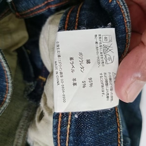Puede incluir: Primer plano de una etiqueta de jeans de mezclilla con texto japon&eacute;s y s&iacute;mbolos de cuidado. La etiqueta indica que los jeans est&aacute;n hechos de 95% algod&oacute;n y 5% poliuretano. La etiqueta tambi&eacute;n indica "MADE IN CHINA".