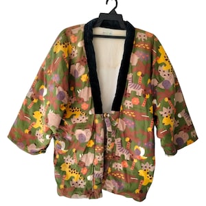 Könnte beinhalten: Eine farbenfrohe Kimono-Jacke mit schwarzem Samtkragen. Die Jacke zeigt ein sich wiederholendes Muster verschiedener Tiere in Gelb-, Braun-, Lila- und Grüntönen. Das Kleidungsstück hängt an einem schwarzen Kleiderbügel vor weißem Hintergrund.