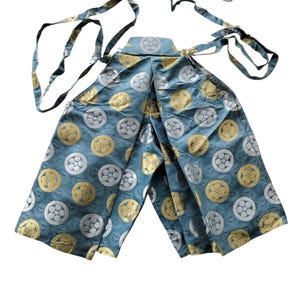 May include: A teal hakama, a traditional Japanese garment, featuring a repeating pattern of gold and silver circular designs. The hakama has long ties and is made of a shiny fabric.