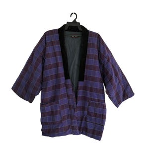 May include: A purple and burgundy plaid kimono-style jacket with a black collar and two front pockets. The jacket is hanging on a black hanger against a white background. The sleeves are three-quarter length.