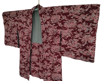 May include: A maroon kimono with a floral pattern, hanging on a hanger. The kimono has long sleeves and a light green lining. The floral pattern includes pink and gray accents, creating a detailed design.