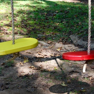 May include: Two wooden swing seats hanging from ropes. The seat on the left is yellow and the seat on the right is red.