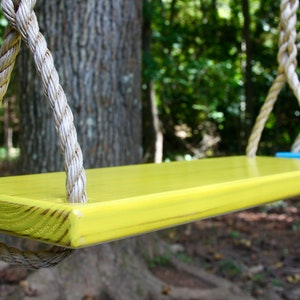May include: A yellow wooden swing set with thick white ropes hanging from a tree branch.
