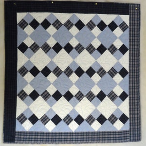 May include: A quilt with a diamond pattern in shades of blue, white, and black. The quilt is quilted with a leaf design.