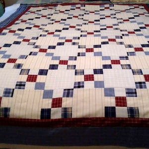 Peut inclure: Une courtepointe avec un motif à carreaux dans des tons de bleu, rouge et blanc. La courtepointe est faite de différents tissus, y compris des motifs à carreaux et à rayures.