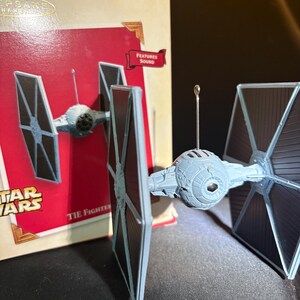 May include: A gray TIE Fighter ornament with black solar panels, a spherical cockpit, and a silver hanger. The ornament is from the Star Wars franchise and has a box that says "Features Sound".