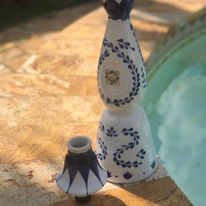 May include: Two white ceramic decorative pieces with blue floral patterns. The taller piece is slender, the smaller is wider. Both have a glossy finish and are on a stone surface. The larger piece is approximately 30 cm tall.