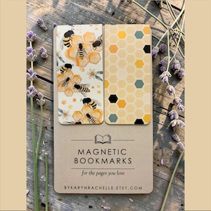 May include: Two rectangular magnetic bookmarks attached to a tan display card. One bookmark features a pattern of bees, honeycombs, and small white flowers. The other displays a geometric honeycomb pattern in yellow, black, and teal. The card reads MAGNETIC BOOKMARKS for the pages you love and BYKARYNRACHELLE.ETSY.COM.