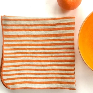 bright orange stripes hand printed on linen napkins, folded and sitting next to a bright orange bowl with a tangerine