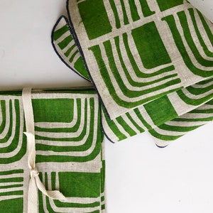 Pode incluir: Conjunto de quatro guardanapos de linho verde com um padr&atilde;o geom&eacute;trico branco. Os guardanapos est&atilde;o dobrados e amarrados com uma fita branca.
