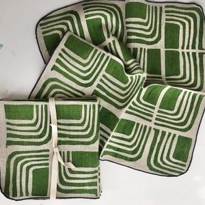 Pode incluir: Conjunto de quatro guardanapos de linho verde e branco com um padr&atilde;o geom&eacute;trico. Os guardanapos est&atilde;o dobrados e amarrados juntos com uma fita branca.