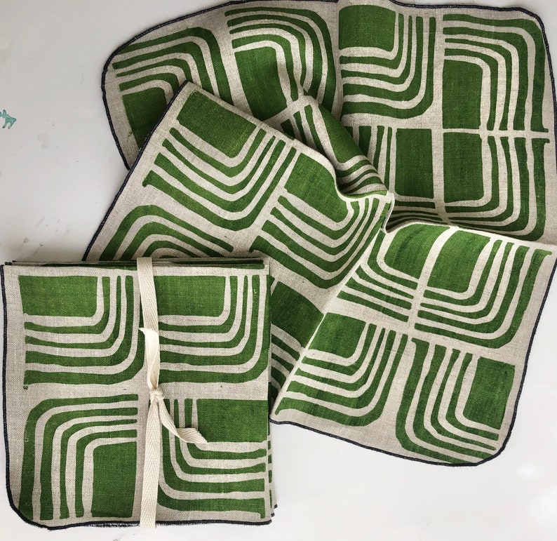 Pode incluir: Conjunto de quatro guardanapos de linho verde e branco com um padr&atilde;o geom&eacute;trico. Os guardanapos est&atilde;o dobrados e amarrados juntos com uma fita branca.