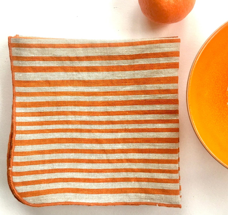 bright orange stripes hand printed on linen napkins, folded and sitting next to a bright orange bowl with a tangerine