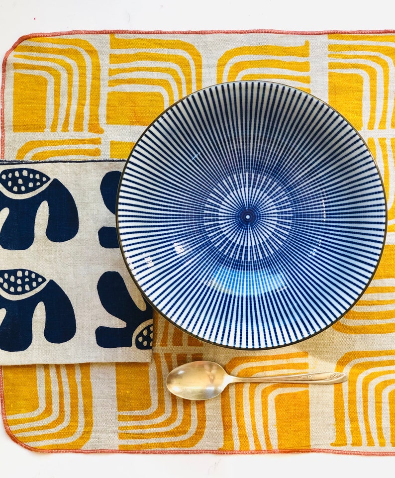 Op de afbeelding: Een blauwe en witte gestreepte keramische kom op een gele en witte gepatroneerde stoffen placemat met een zilveren lepel.