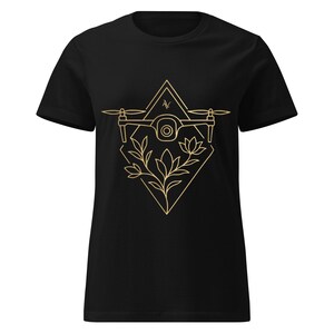Op de afbeelding: Zwart t-shirt met een goudkleurig drone-ontwerp en bloemaccenten. De drone staat in een ruit, met een driehoek erboven. Het ontwerp is in een lijntekeningstijl.