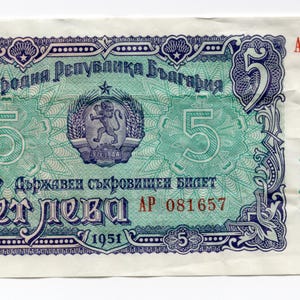 May include: A Bulgarian 5 Leva banknote from 1951. The note features green and purple ornate designs, the number 5, and text in Cyrillic script. The serial number AP 081657 is printed in red.