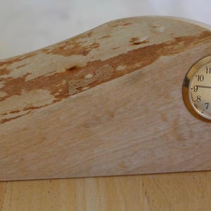 May include: A wooden desk clock with a light brown finish and a gold-colored clock face. The clock has a curved design with a natural wood grain pattern and measures approximately 8 inches long.
