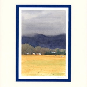 May include: A watercolor painting of a rural landscape with a field in the foreground, a line of trees in the middle ground, and a mountain range in the background. The sky is overcast and gray. The painting is framed in a dark blue frame.