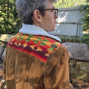 May include: A brown corduroy jacket featuring a white sherpa collar and a vibrant, multi-colored geometric patterned yoke across the shoulders. The jacket has a textured corduroy fabric and a soft, plush white lining visible at the collar.