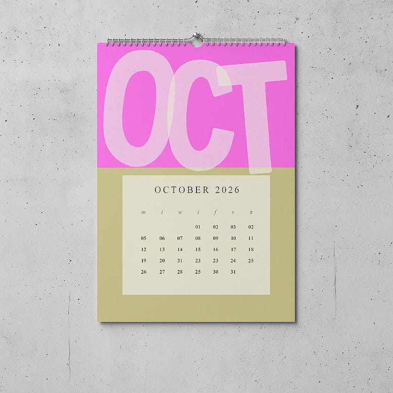 May include: A wall calendar for October 2026. The top section is bright pink with the large word "OCT" in white. The bottom section is a muted green with the month's calendar grid. The calendar is hanging on a wall.