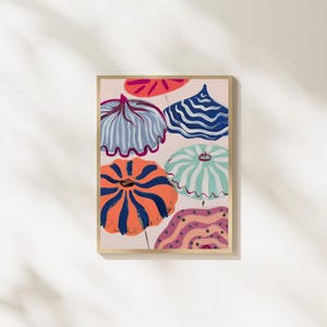May include: A framed art print featuring a colorful abstract design of beach umbrellas. The umbrellas have various patterns, including stripes and wavy lines, in shades of blue, orange, and pink. The artwork is set against a light pink background.