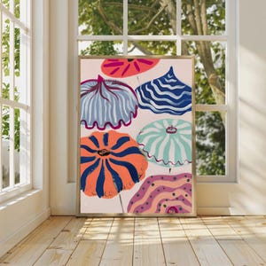 May include: A framed abstract art print featuring colorful umbrella-like shapes in shades of orange, blue, pink, and teal. The artwork has a light pink background and is displayed in a room with natural light.