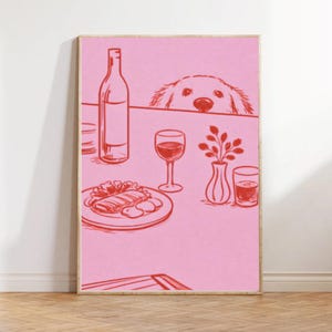 May include: Pink and red illustration of a dining scene. A wine bottle, glass of wine, plate of food, and a vase with a plant are on a table. A dog's face peeks over the table's edge. The artwork is framed.