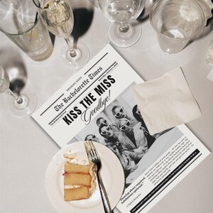 Könnte beinhalten: Eine schwarz-weiße Zeitung mit dem Titel "The Bachelorette Times" und der Schlagzeile "KISS THE MISS Goodbye!" liegt auf einem Tisch. Ein Teller mit Kuchen und einer Gabel, Gläser und eine Serviette sind ebenfalls vorhanden. Die Zeitung zeigt ein Foto von Frauen mit herzförmigen Sonnenbrillen.