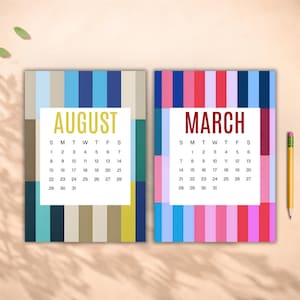 May include: Two colorful calendars, one for August and one for March, are displayed. The August calendar has vertical stripes in shades of blue, teal, and gold. The March calendar has pink, red, and blue stripes. A pencil rests on the side.