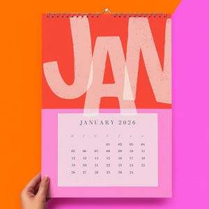 May include: A wall calendar for January 2026, featuring a bold design with the month's name in large, white letters against a red background. The calendar has a pink lower section with the days of the month.