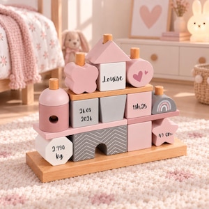 Peut inclure: Un jouet à empiler en bois composé de formes géométriques variées dans des tons rose, blanc et gris. Les blocs sont personnalisés avec le prénom Louise, la date 26.08.2026, l'heure 18h25, le poids 2.990 kg et la taille 49 cm, avec un arc-en-ciel.