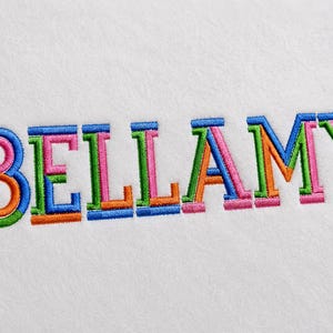 Puede incluir: El nombre BELLAMY está bordado en letras mayúsculas sobre una superficie de tela blanca. Cada letra presenta un diseño de varias capas con hilos de colores vibrantes y contrastantes, incluyendo azul, rosa, verde y naranja, creando un efecto.