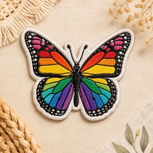 May include: Embroidered butterfly patch with a rainbow gradient design. The butterfly has a white border and black detailing on the wings. The wings feature a spectrum of colors, including pink, red, orange, yellow, green, blue, and purple.