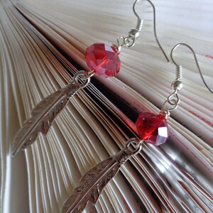 May include: A pair of silver earrings with red crystal beads and feather charms.