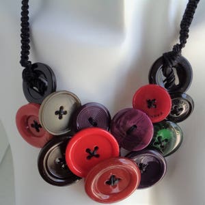 May include: A necklace made of various colored buttons, including red, black, purple, and green. The buttons are strung together on a black cord.