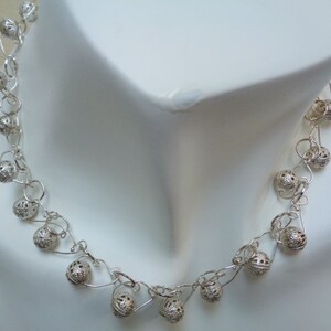 May include: A silver necklace with delicate chain links and small, round, openwork beads. The necklace is displayed on a white mannequin.