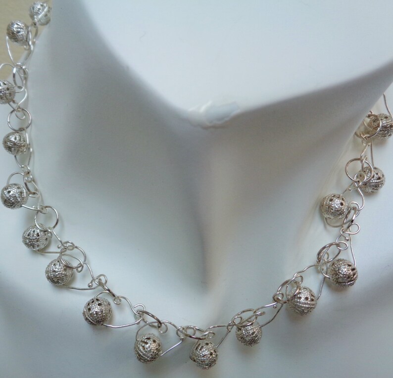 May include: A silver necklace with delicate chain links and small, round, openwork beads. The necklace is displayed on a white mannequin.