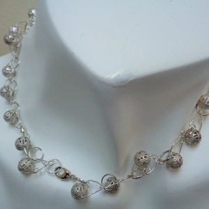 May include: A silver necklace with a delicate chain and small, openwork ball charms.