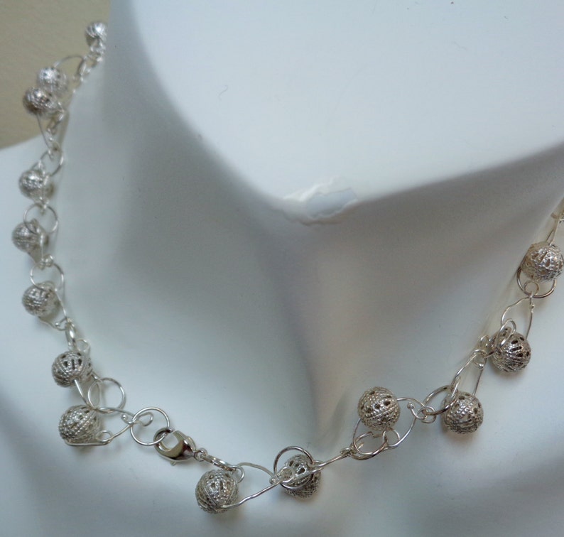May include: A silver necklace with a delicate chain and small, openwork ball charms.
