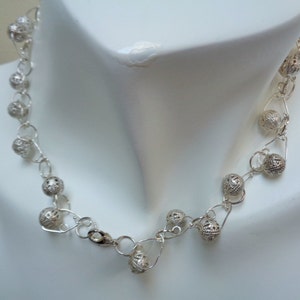 May include: A silver necklace with delicate, openwork ball charms. The necklace is made of fine silver wire and features a simple clasp.