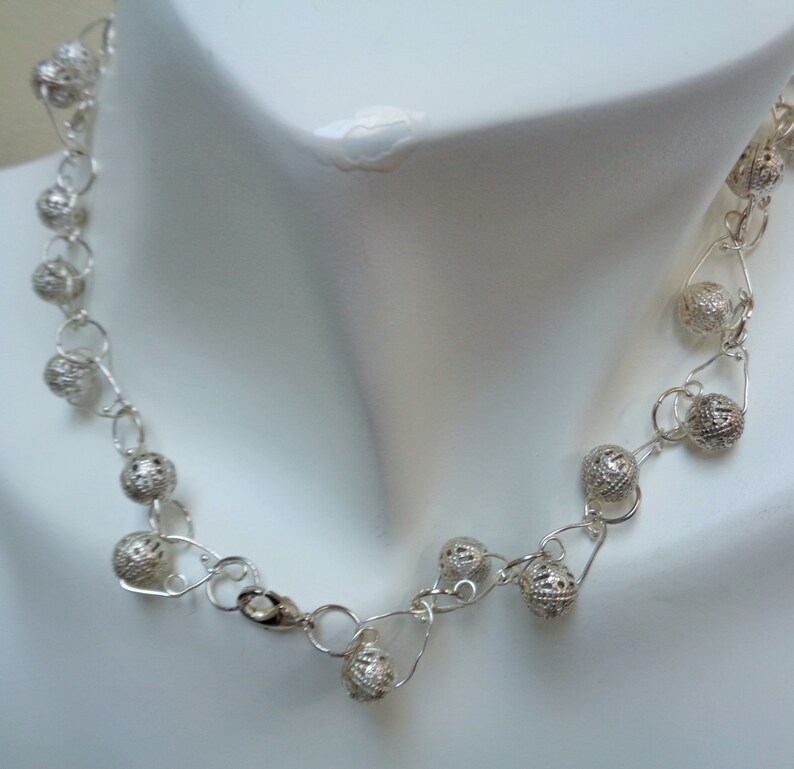 May include: A silver necklace with delicate, openwork ball charms. The necklace is made of fine silver wire and features a simple clasp.