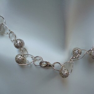 May include: A silver necklace with a delicate chain and openwork ball charms. The necklace has a lobster clasp closure.