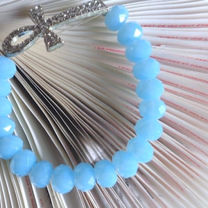 May include: A light blue crystal bead bracelet with a silver ankh charm. The bracelet is on a white background.