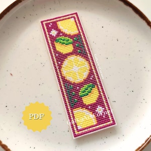 May include: A rectangular bookmark with a cross-stitch design featuring yellow lemons, green leaves, and white flowers on a burgundy background. The bookmark has a white border and the text "PDF" on a yellow starburst.